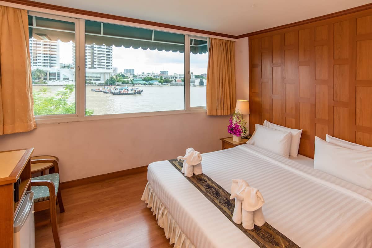 A hotel room with a large window, a bed with white linens, a wooden desk, and a chair.