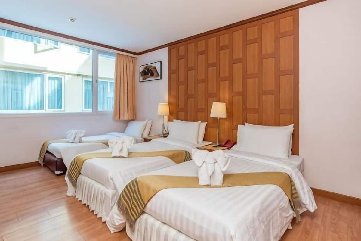 A hotel room with three beds, wooden headboard, two bedside lamps, and a window with curtains.