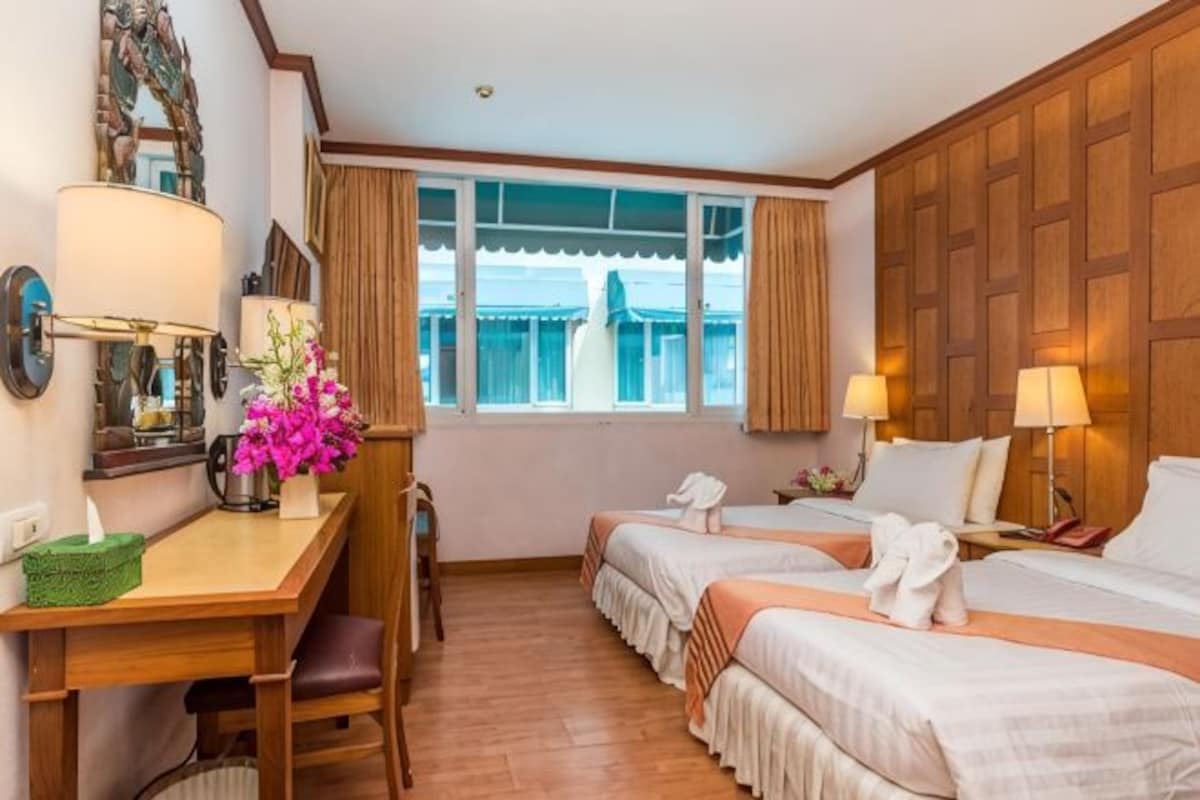Une chambre d’hôtel avec deux lits, un bureau avec une lampe, une chaise, une fenêtre avec des rideaux et un lambris en bois.