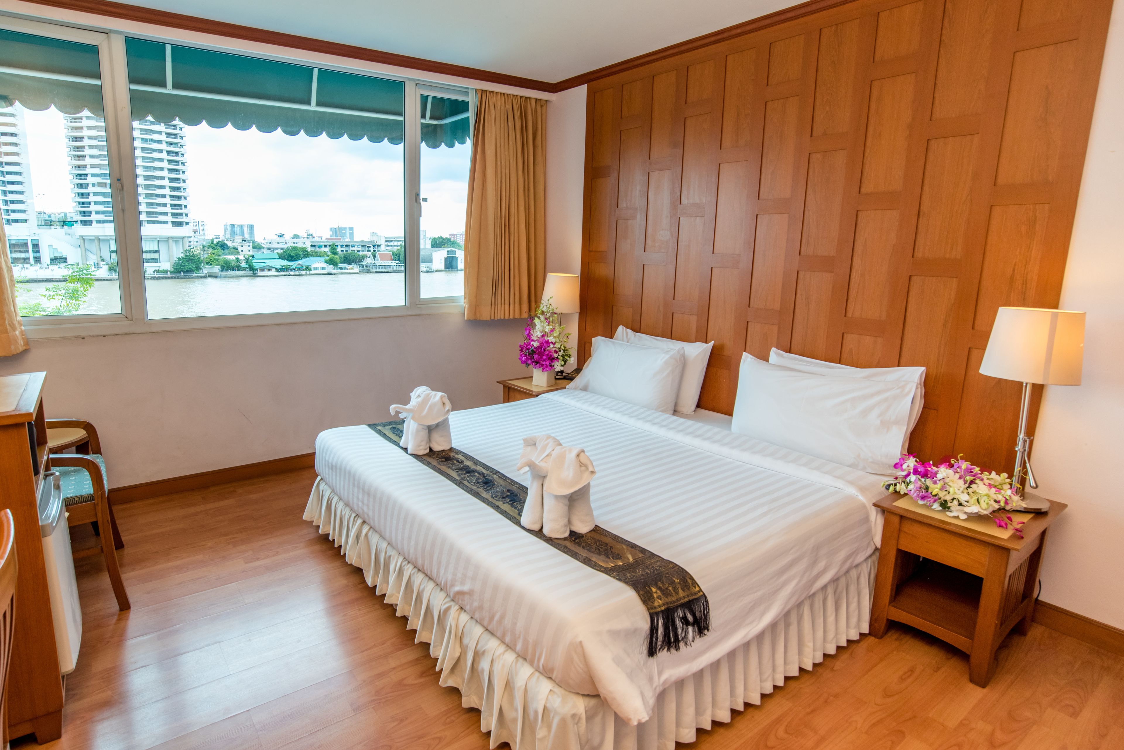 A hotel room with a large bed, wooden paneling, a view of the city, and a desk with a chair.
