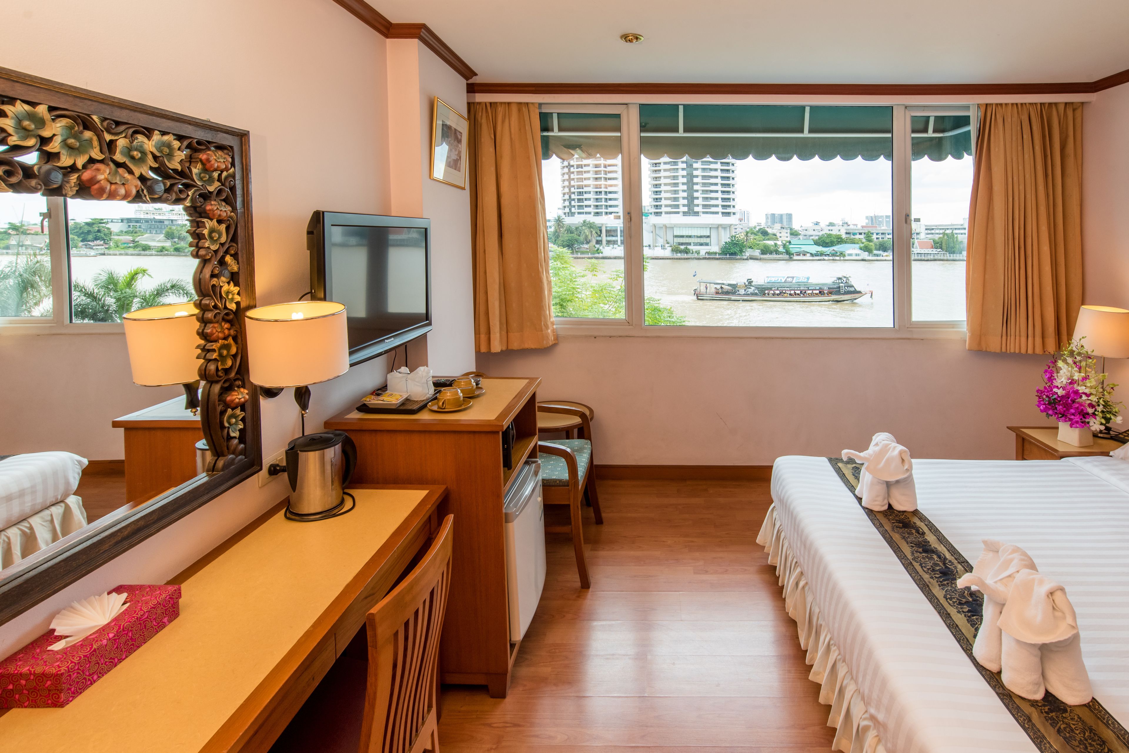 A hotel room with a bed, a desk, a television, a window with a view of a river and buildings, and a bathroom.