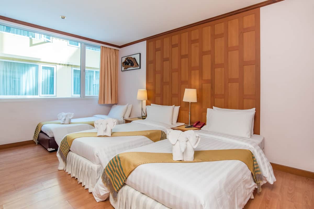 A hotel room with three beds, wooden paneling on the wall, and a large window with curtains.