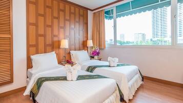 A hotel room with two beds, wooden paneling on the wall, a window with a view of buildings, and a flower vase on the nightstand.