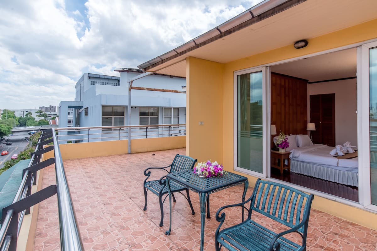 A balcony with two chairs and a table, a sliding glass door leading to a bedroom, and a cityscape view.