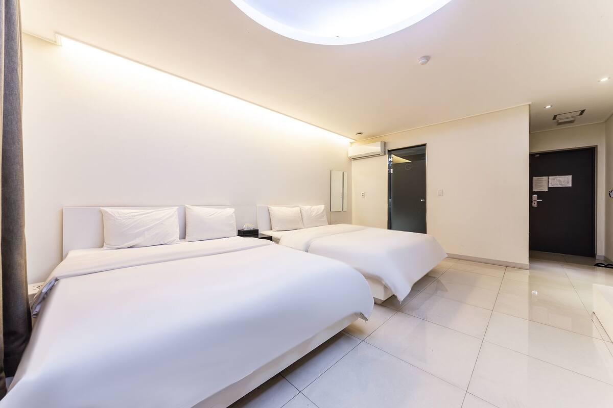 A hotel room with two beds, a skylight, a door, and a tiled floor.