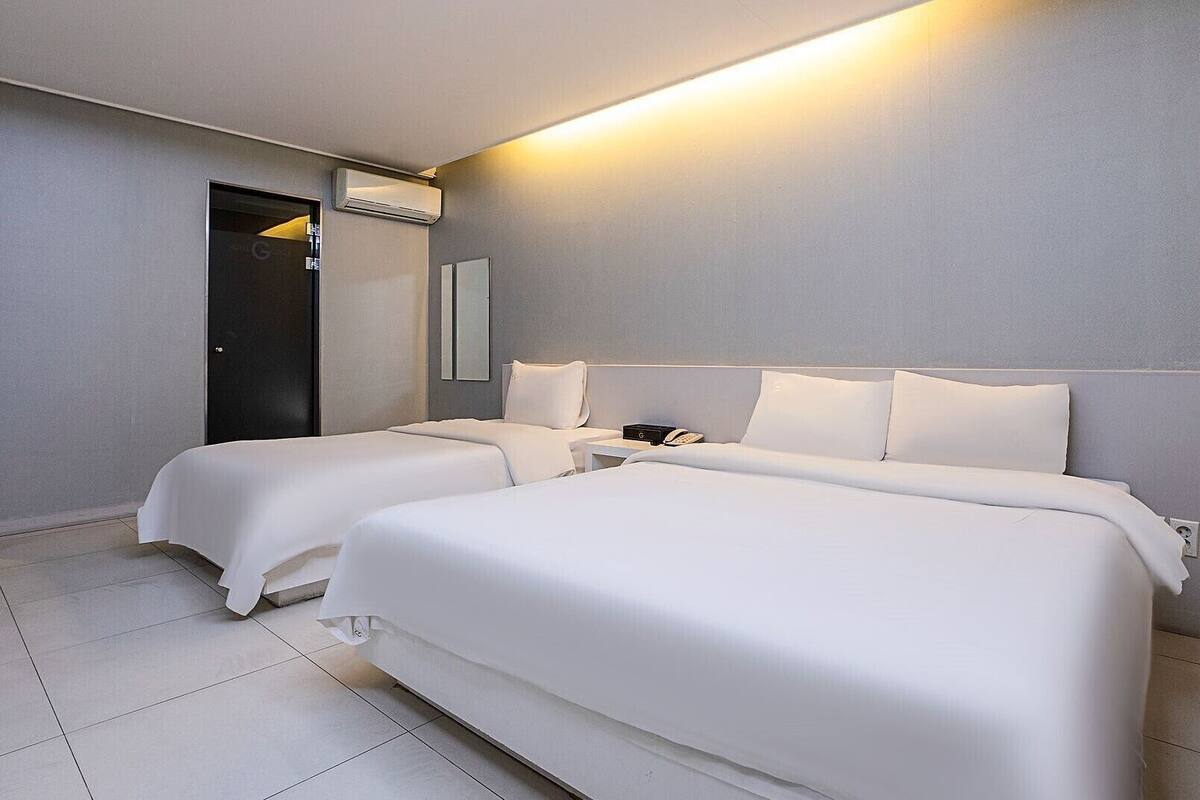 A hotel room with two beds, a bedside table with a phone, and an air conditioning unit.