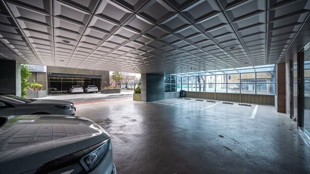 Un espacio interior amplio con un diseño de techo moderno, ventanas grandes y un estacionamiento con coches.