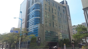 Un hotel moderno con un llamativo letrero que dice 'HOTEL RUBY', con fachada de vidrio y entrada a un estacionamiento.