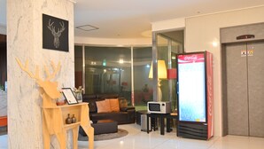 Un vestíbulo moderno con una columna de mármol, un sofá, un televisor y un refrigerador Coca-Cola.