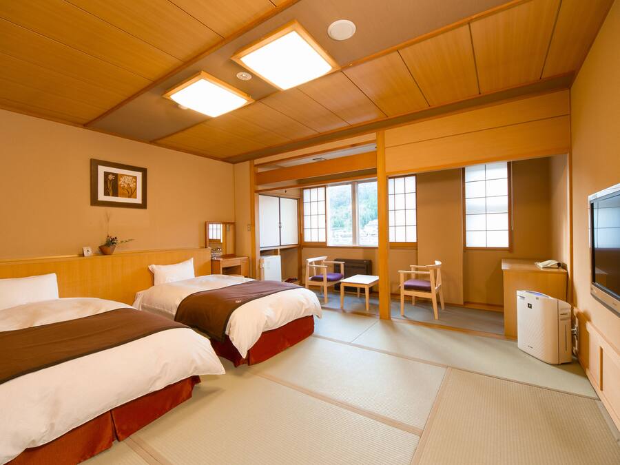 Une chambre d’hôtel avec deux lits, un bureau, une chaise, une télévision et une fenêtre donnant sur des arbres.