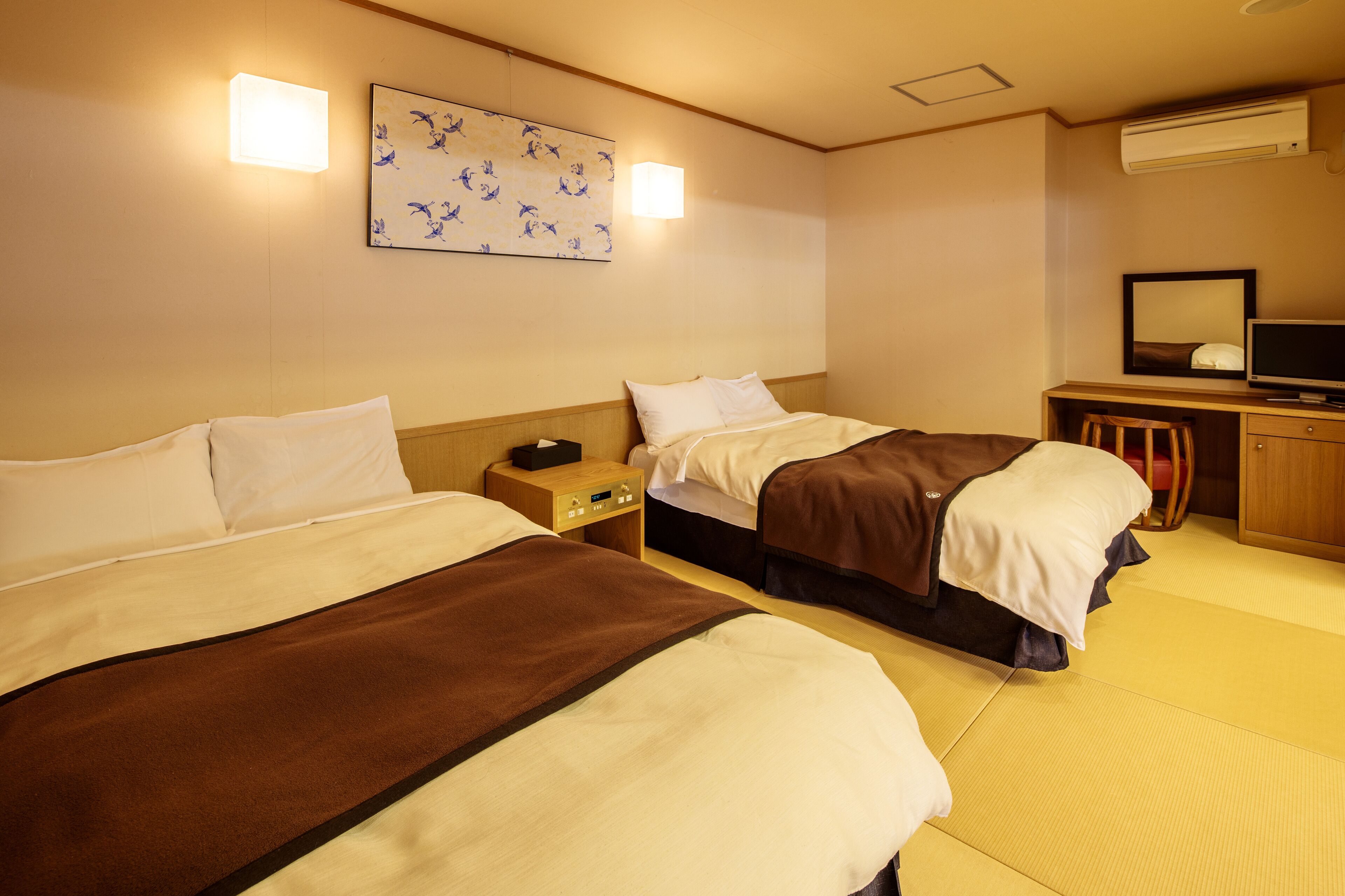 A hotel room with two beds, a desk with a television, and a wall-mounted air conditioner.