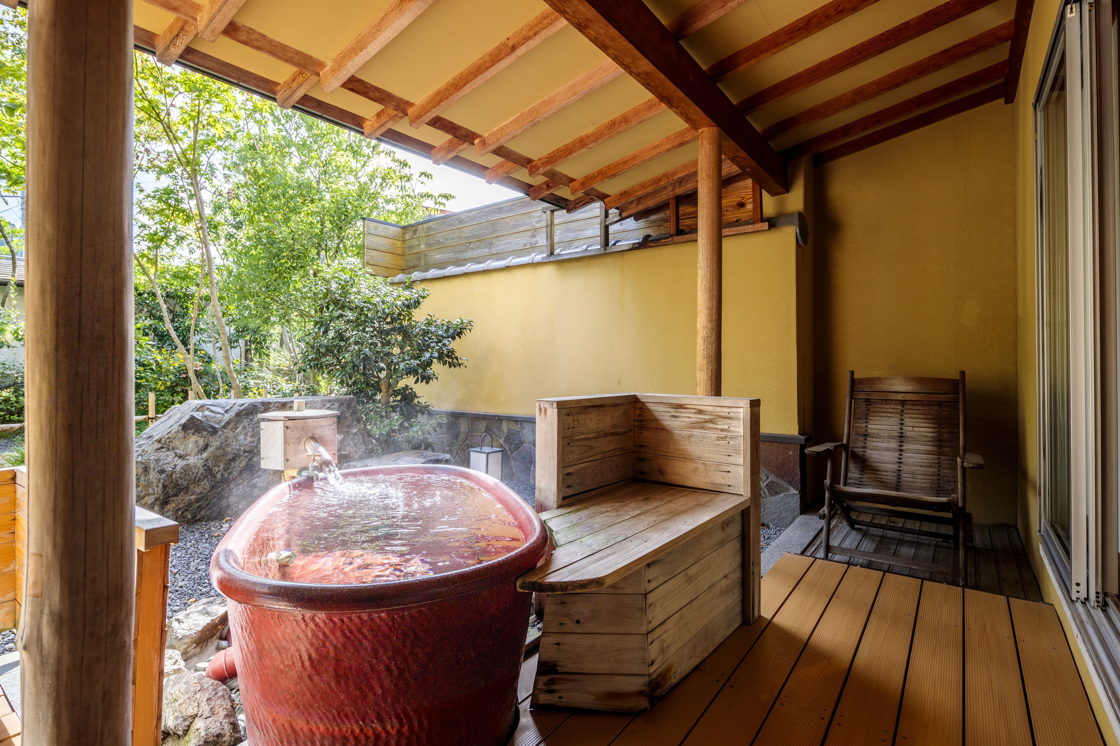 Eine Holzterrasse mit Whirlpool, Holzbanken und einer Steinmauer.