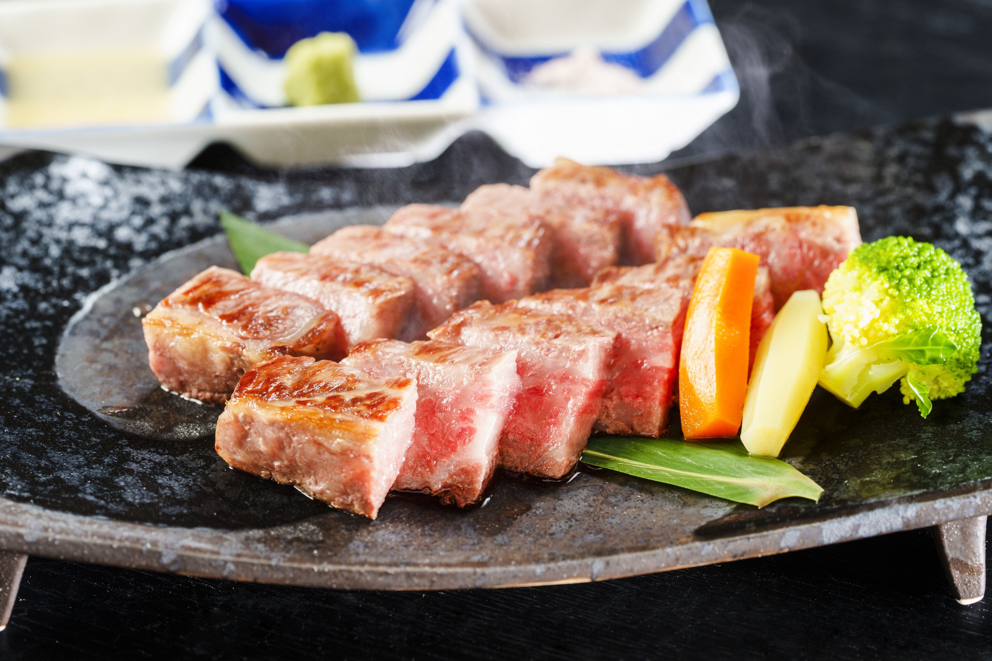 A plate with sliced meat, vegetables, and a green garnish on a dark surface.