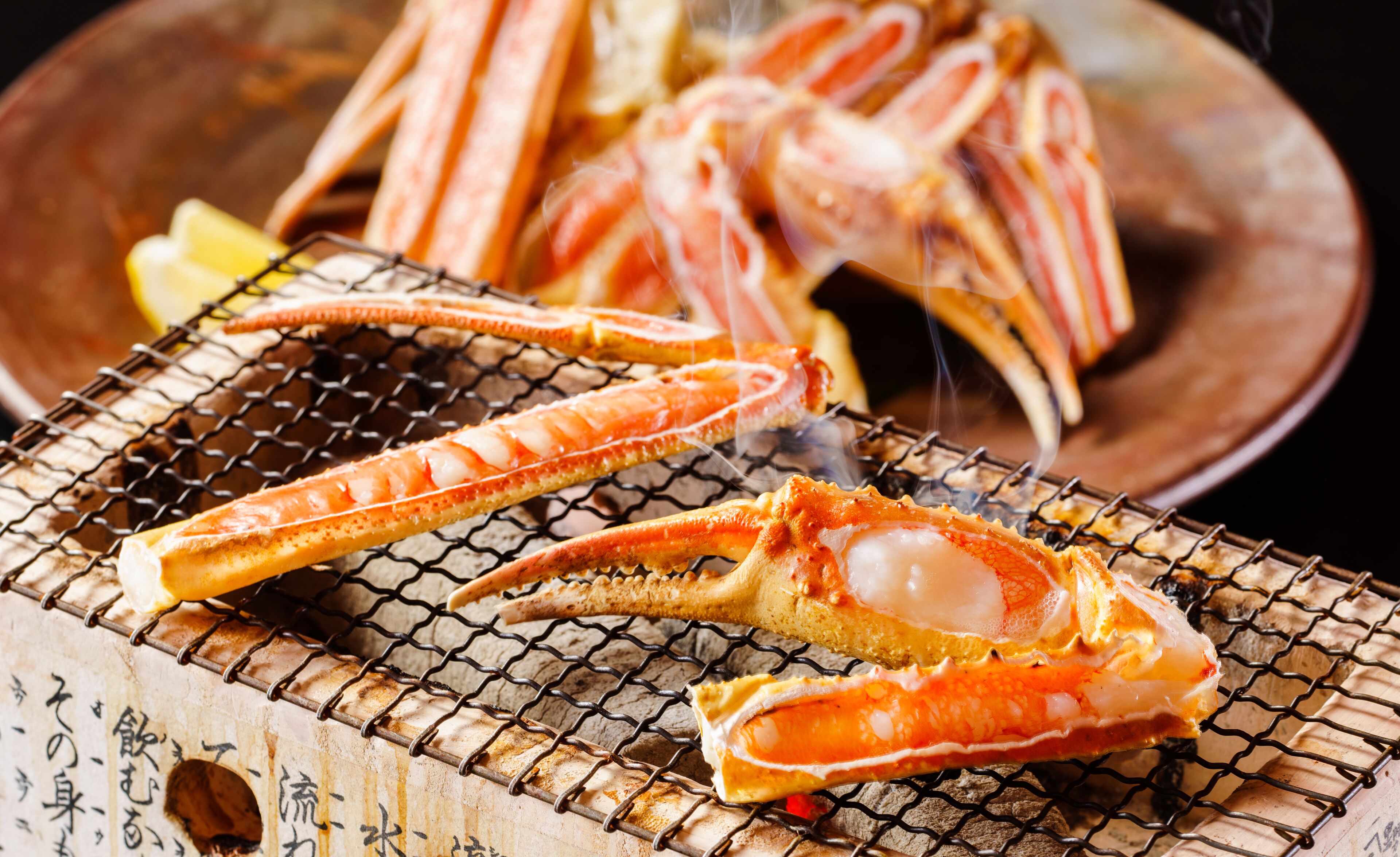 A grill with seafood, including crab legs, on a wooden surface with Japanese characters.