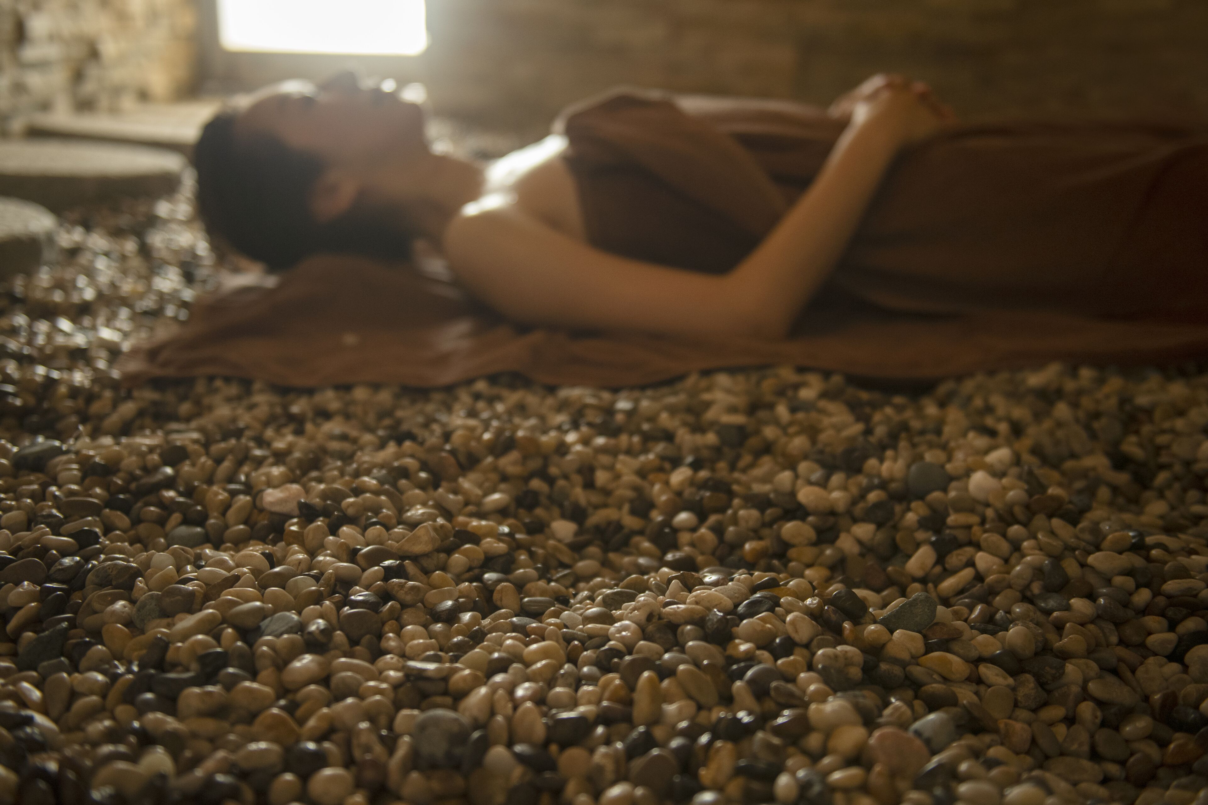 Una persona acostada sobre una cama cubierta con una manta, rodeada de piedras.