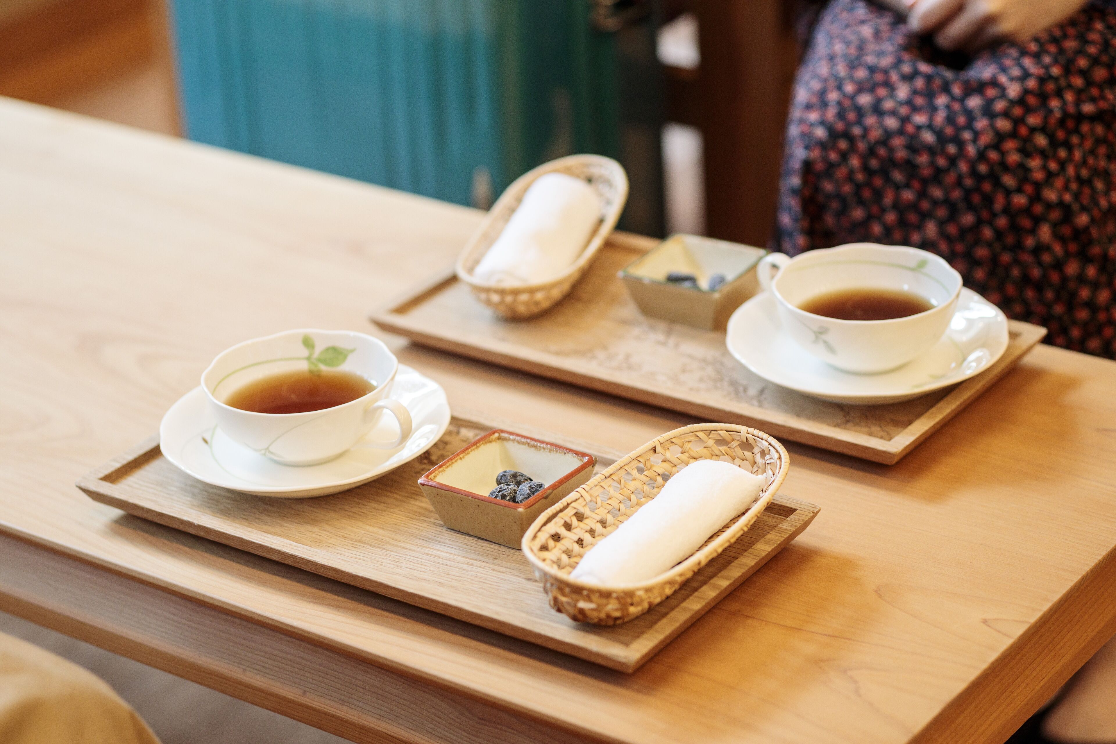 A tray with a cup of tea, a small bowl of blueberries, and a woven basket with a rolled-up item on a wooden table.