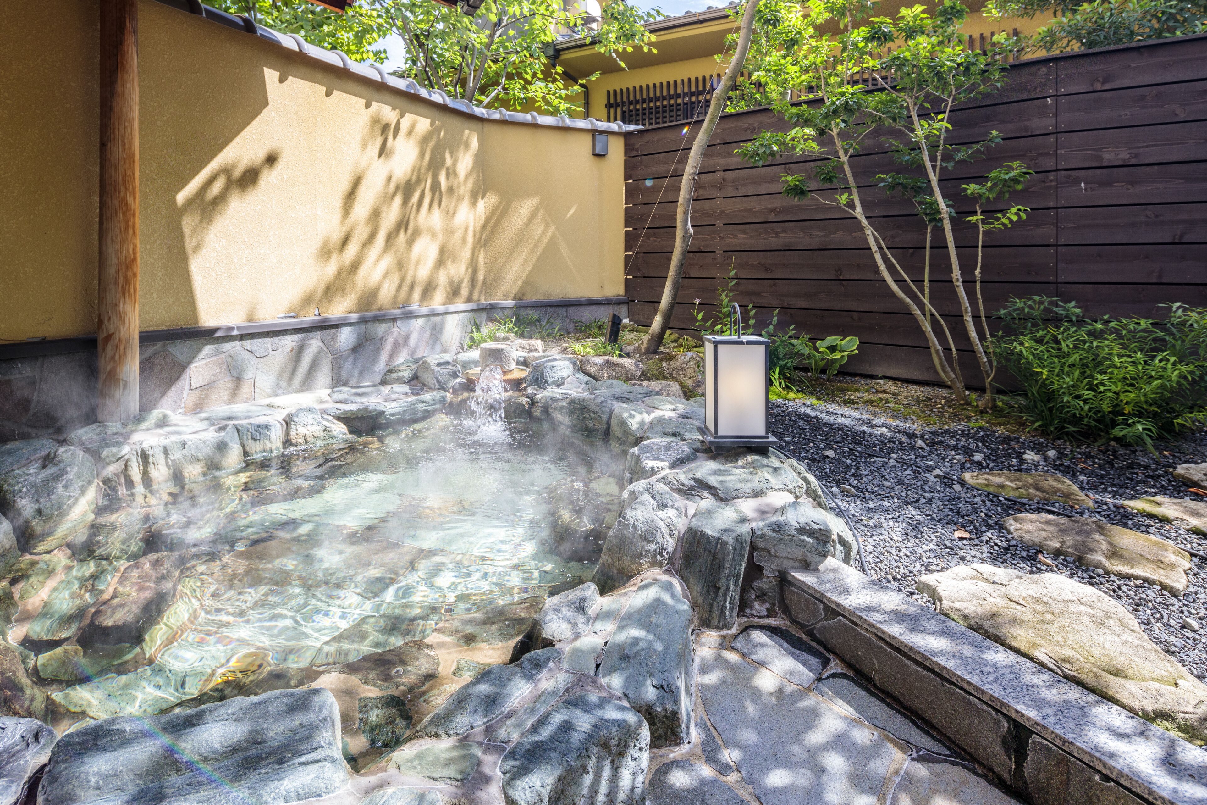 A hot spring area with a stone pool, surrounded by a wooden fence and greenery.