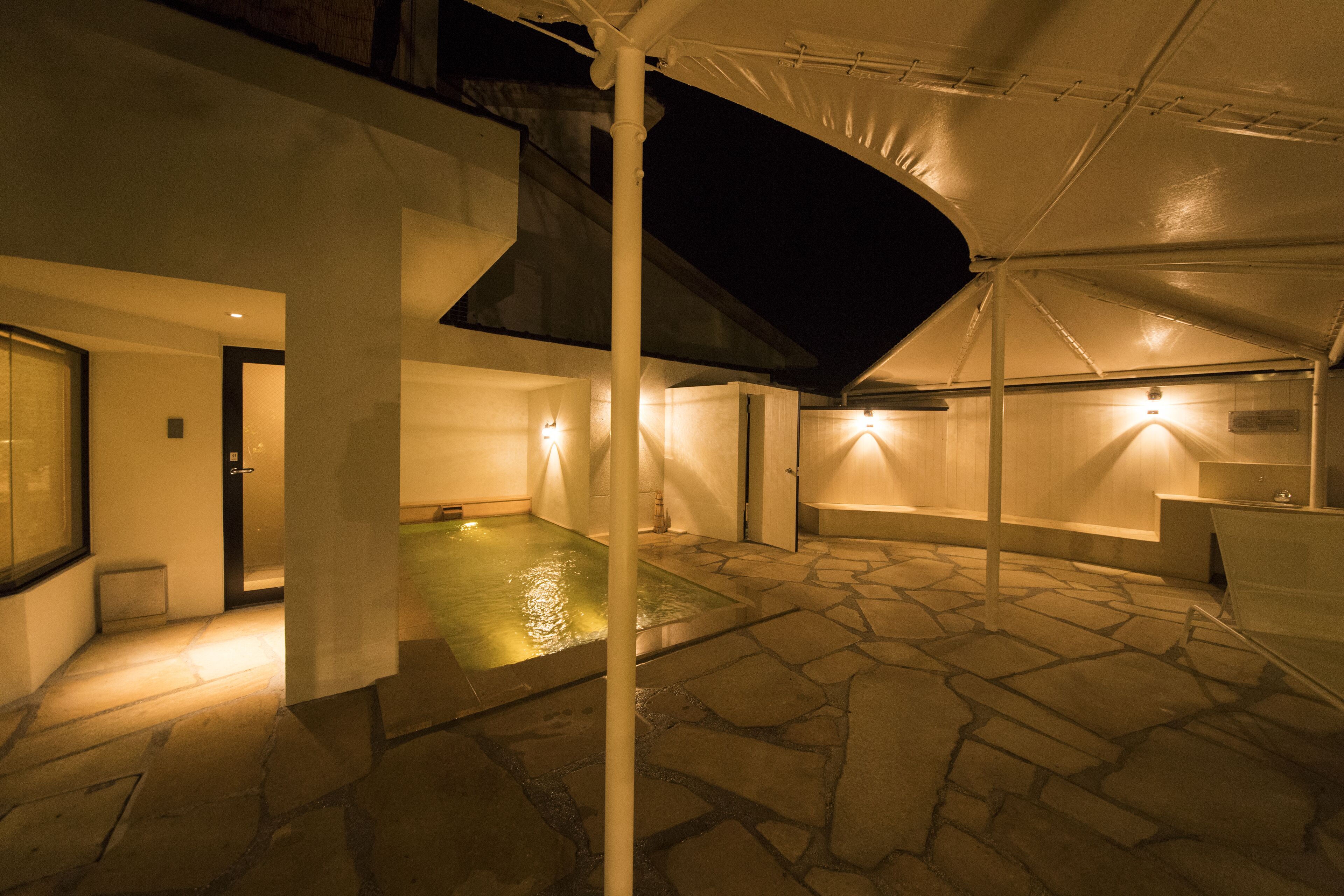 A covered outdoor area with a stone floor, a small pool, and a white umbrella structure.