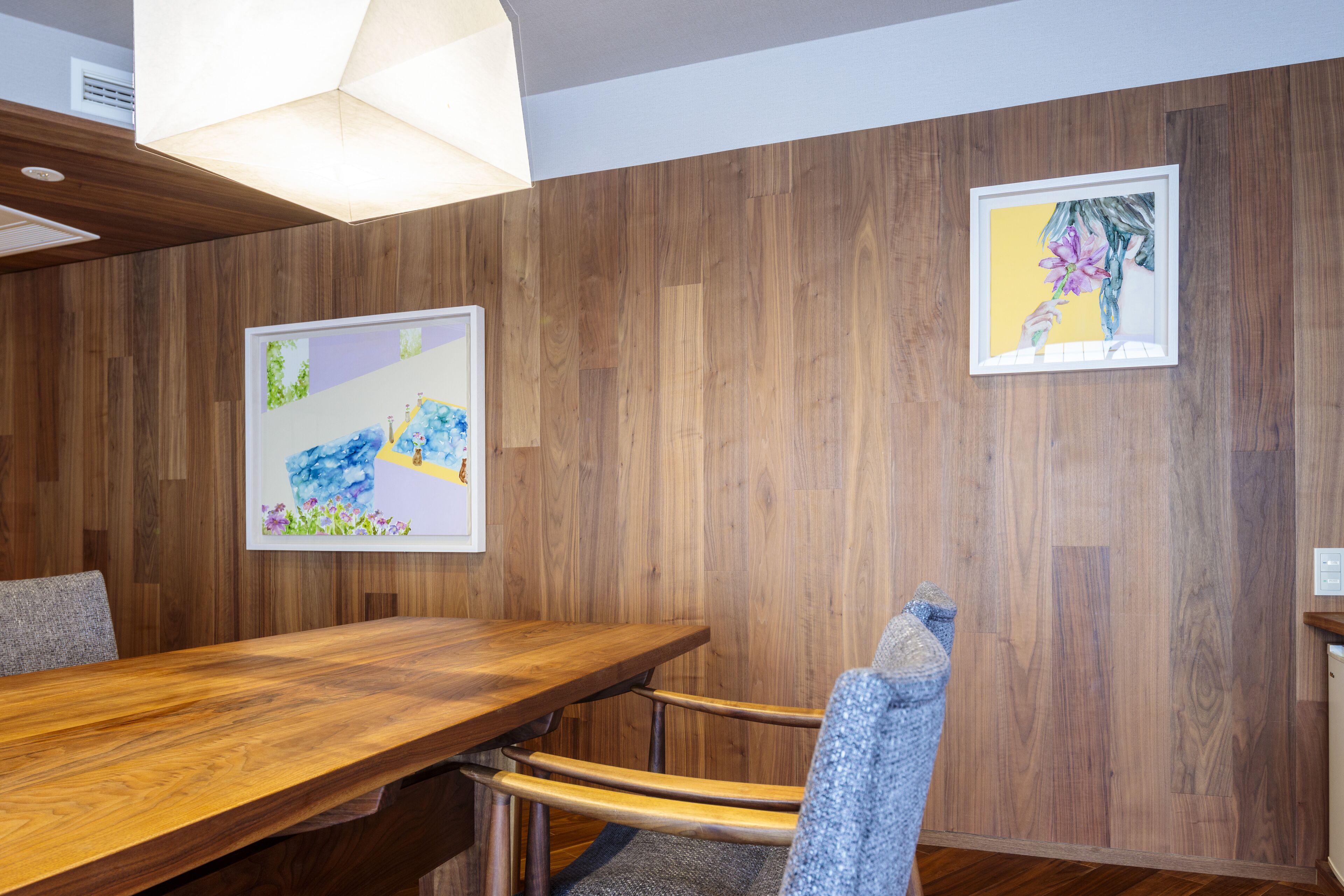 Un salón de conferencias con una mesa y sillas de madera, dos cuadros enmarcados en la pared y una lámpara en el techo.
