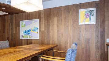 Un salón de conferencias con una mesa y sillas de madera, dos cuadros enmarcados en la pared y una lámpara en el techo.