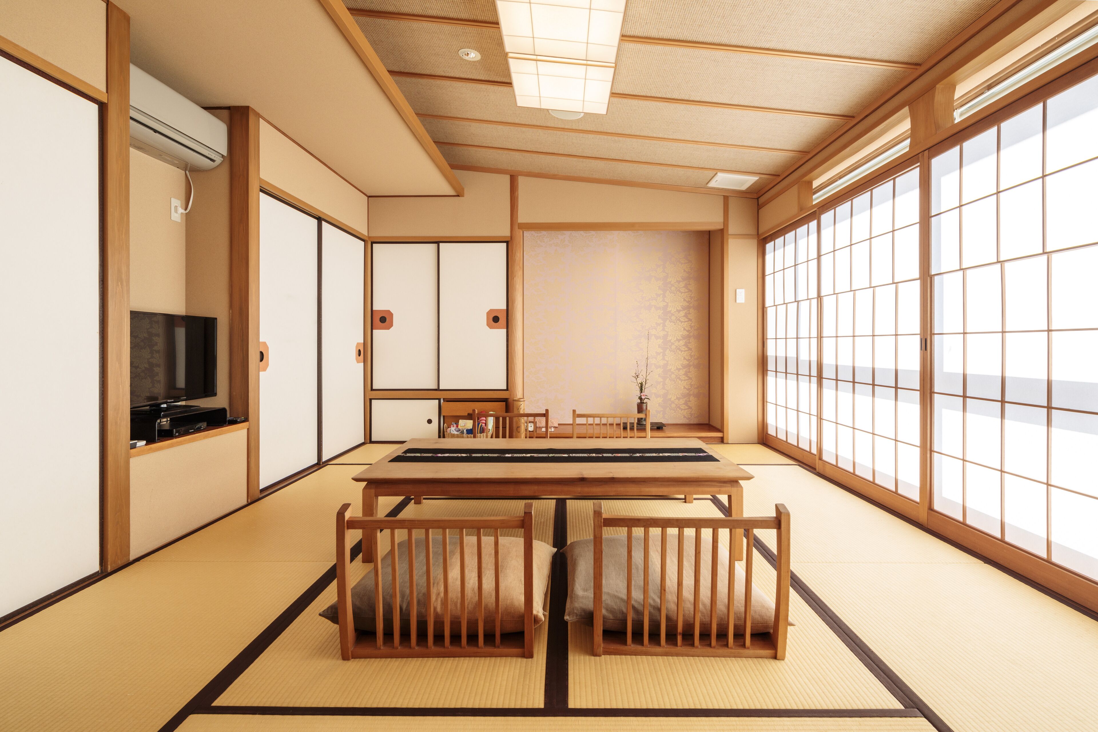 Una habitación japonesa tradicional con suelo de tatami, una mesa baja, cojines, puertas correderas y un televisor.