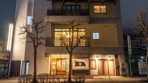 A multi-story building with a ground-level entrance, balconies, and a visible restaurant sign. - Guest House Ouka - Hostel (Takayama)