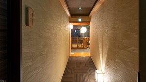 A hallway with patterned walls and a wooden floor, leading to a room with a visible door and a hanging light fixture. - Guest House Ouka - Hostel (Takayama)