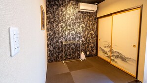 A room with tatami flooring, a shoji screen door, a wall-mounted air conditioner, and a small shelf with a water bottle. - Guest House Ouka - Hostel (Takayama)