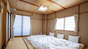 A traditional Japanese room with tatami flooring, a futon bed, sliding doors, and a ceiling fan. - Guest House Ouka - Hostel (Takayama)