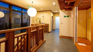 A hotel corridor with wooden railings, a polished stone floor, and a bright pendant light. - Guest House Ouka - Hostel (Takayama)