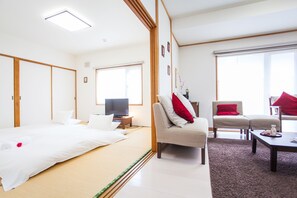 A hotel room with a bed, a television, a sofa, and a coffee table. - Yume House (Kutchan)
