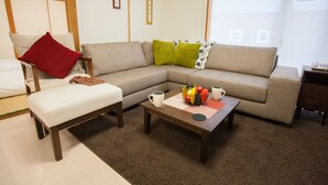 Ein Wohnzimmer mit einer Couch, einer Bank, einem Couchtisch mit Früchten und Tassen sowie einem Fenster mit Aussicht.