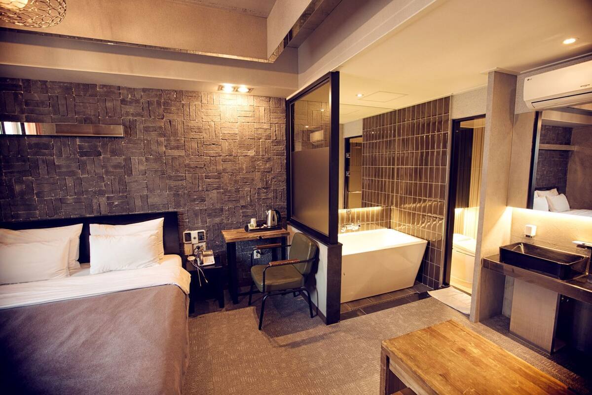 A hotel room with a bed, desk, chair, and a large mirror.