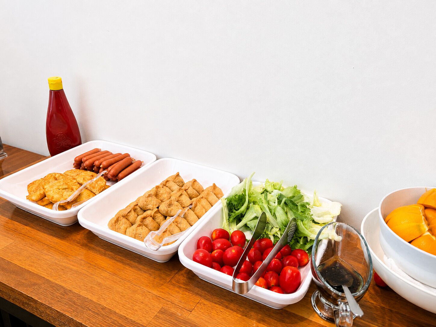 Ein reichhaltiges Buffet mit verschiedenen Speisen, darunter Hotdogs, Gebäck und frisches Gemüse.