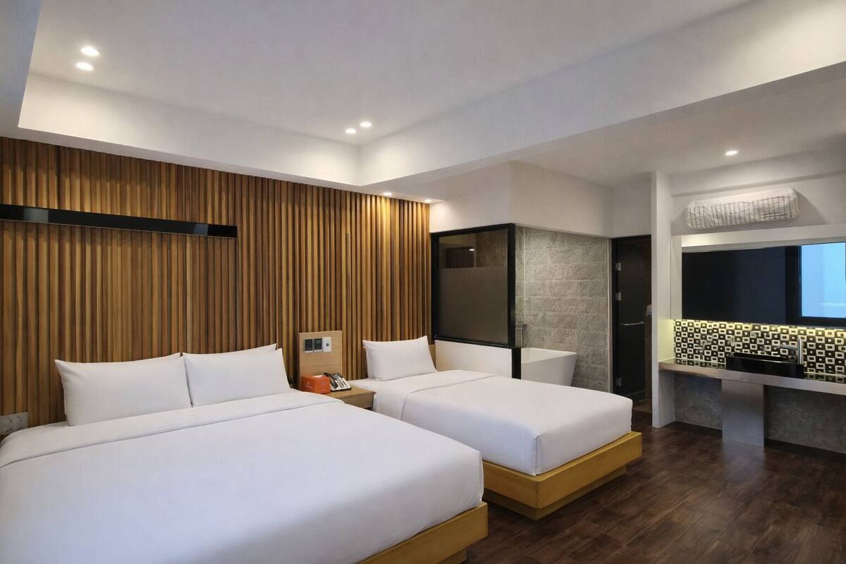 A modern hotel room with two beds, a wooden accent wall, a shower area, and a small kitchenette.