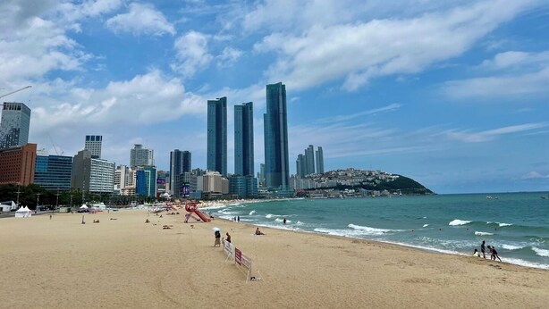 A beach with a city skyline in the background, including tall buildings and a hill. - Haerium Hotel (Busan)