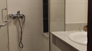 Uma casa de banho moderna com cabine de duche em vidro, lavatório branco e soalho em madeira escura.