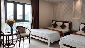 Quarto de hotel com duas camas, uma cadeira, uma mesinha com um vaso e uma janela com cortinas.