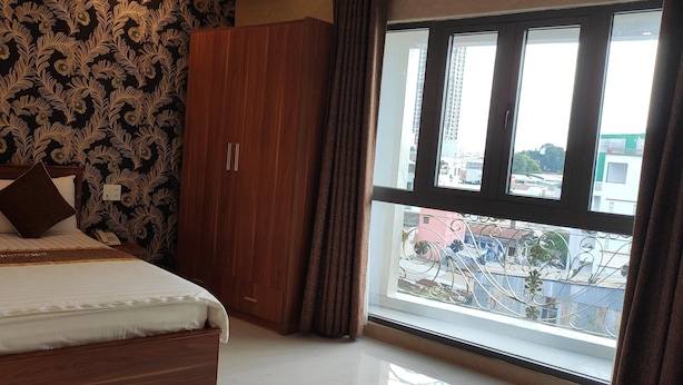 Quarto de hotel com uma cama grande, um guarda-roupa e uma janela com vista para edifícios.