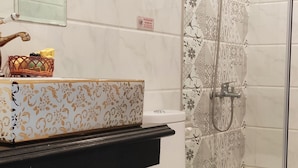 Um banheiro com vaso sanitário branco, box de chuveiro em vidro e toucador com revestimento de azulejos estampados.
