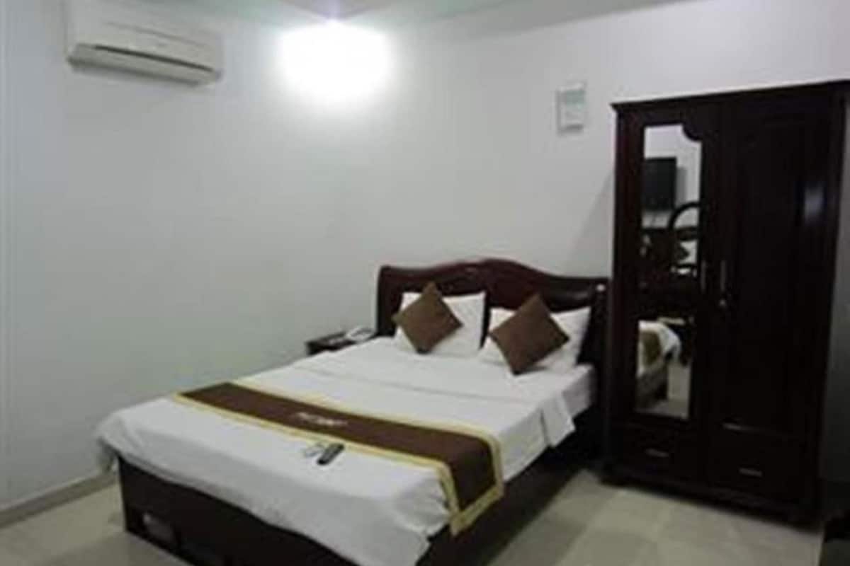 A single bed with a white and brown bedspread, a wooden headboard, and a dark wardrobe.