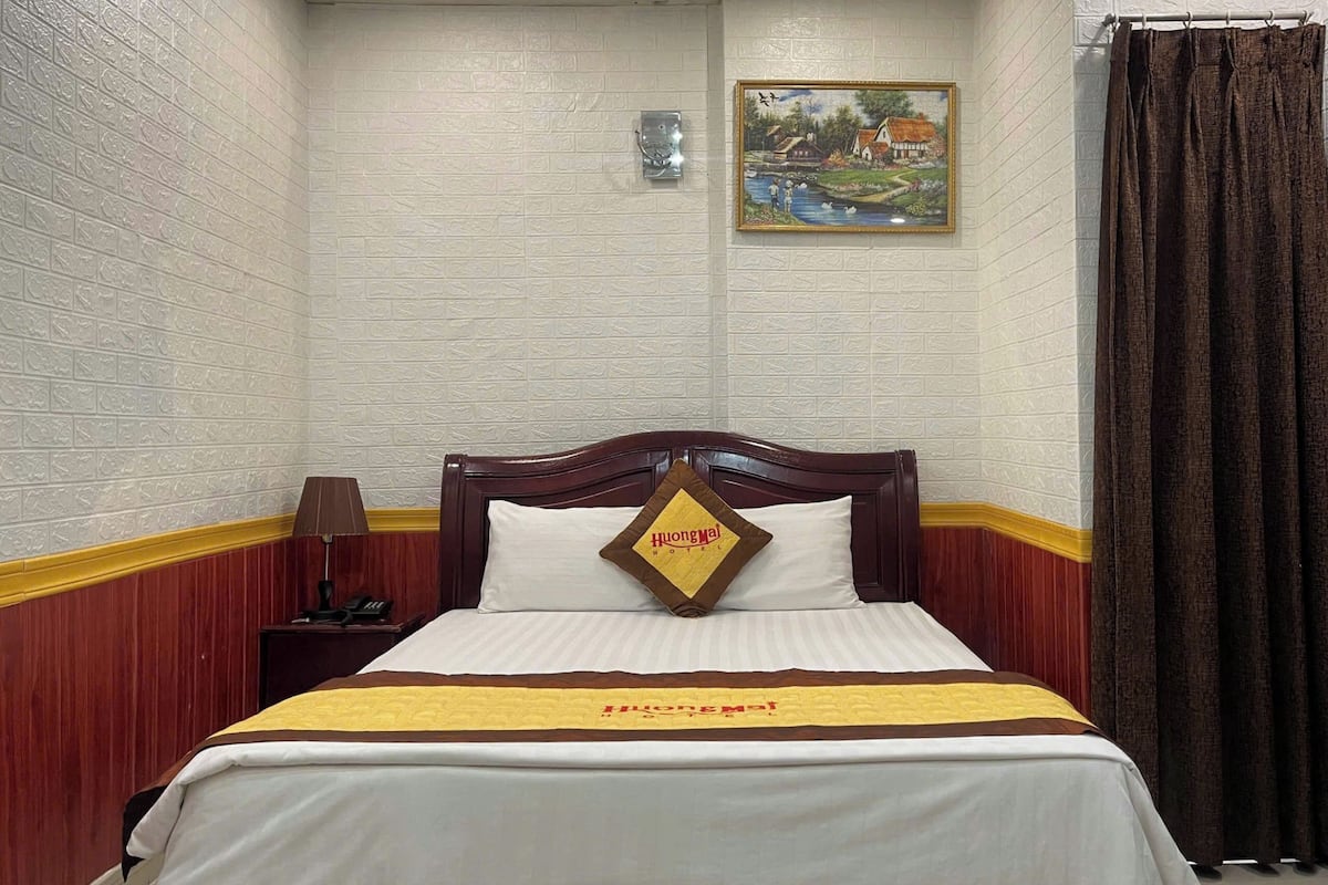 A hotel room with a bed, a nightstand, a lamp, a painting on the wall, and a curtain.