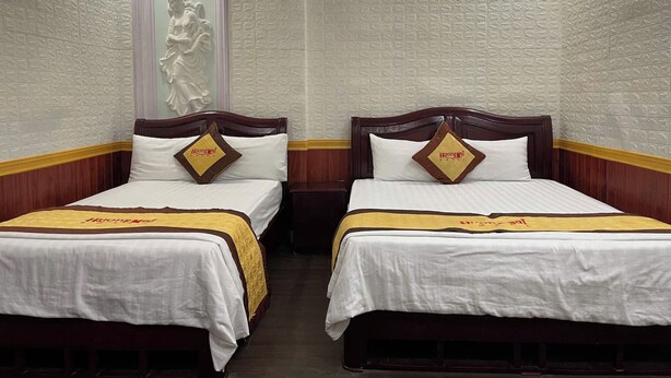 Two single beds with wooden headboards and white bedding, each with a pillow featuring the hotel logo. - Huong Mai 2 Hotel (Ho Chi Minh City)