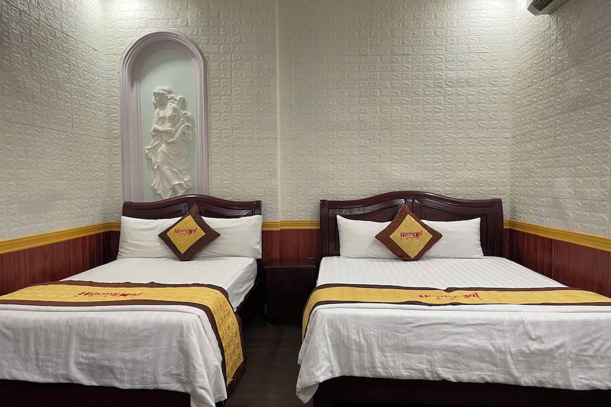Two single beds with wooden headboards and white bedding, each with a pillow featuring the hotel logo.