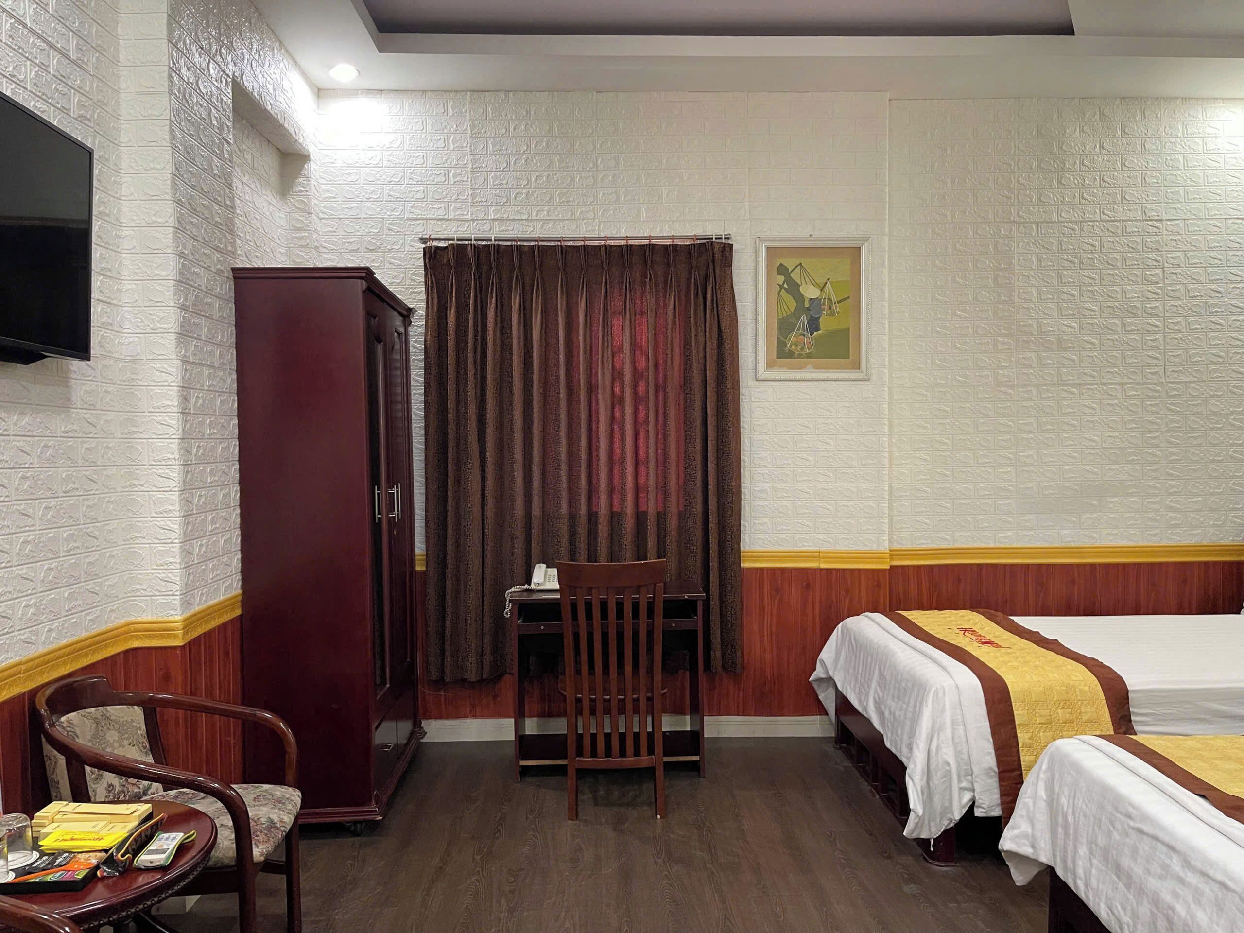 Camera d'albergo con una scrivania in legno, due letti con copripiumini bianchi e gialli, un armadio in legno, una televisione a parete e un quadro incorniciato.