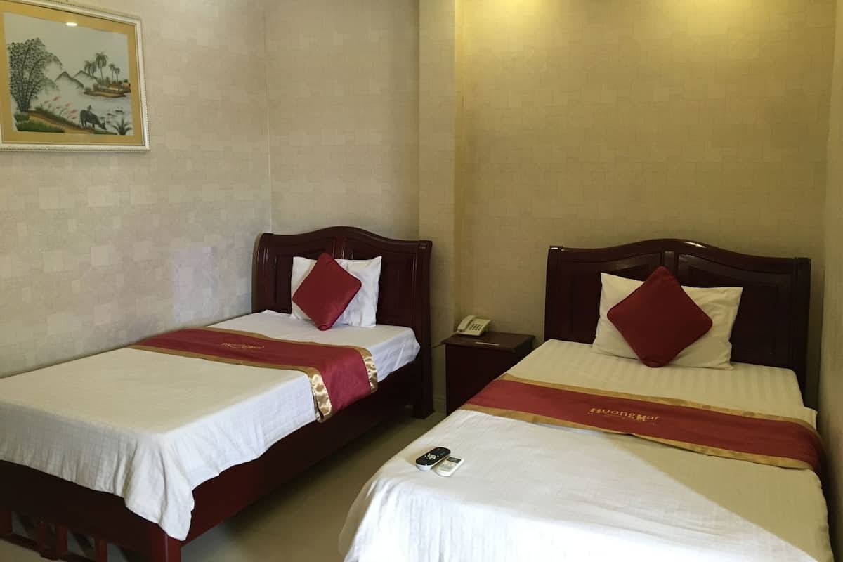 Two single beds with wooden headboards, white linens, red decorative pillows, and a red and gold bedspread.