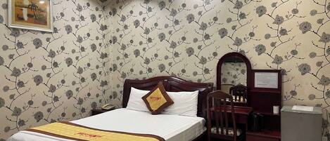 A hotel room with a bed, a desk, a chair, a mirror, and a small refrigerator.