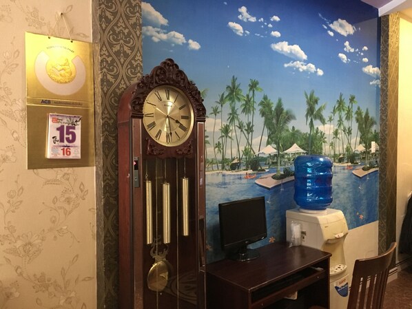 Une pièce avec une grande horloge murale, un ordinateur de bureau et un tableau représentant une plage tropicale.