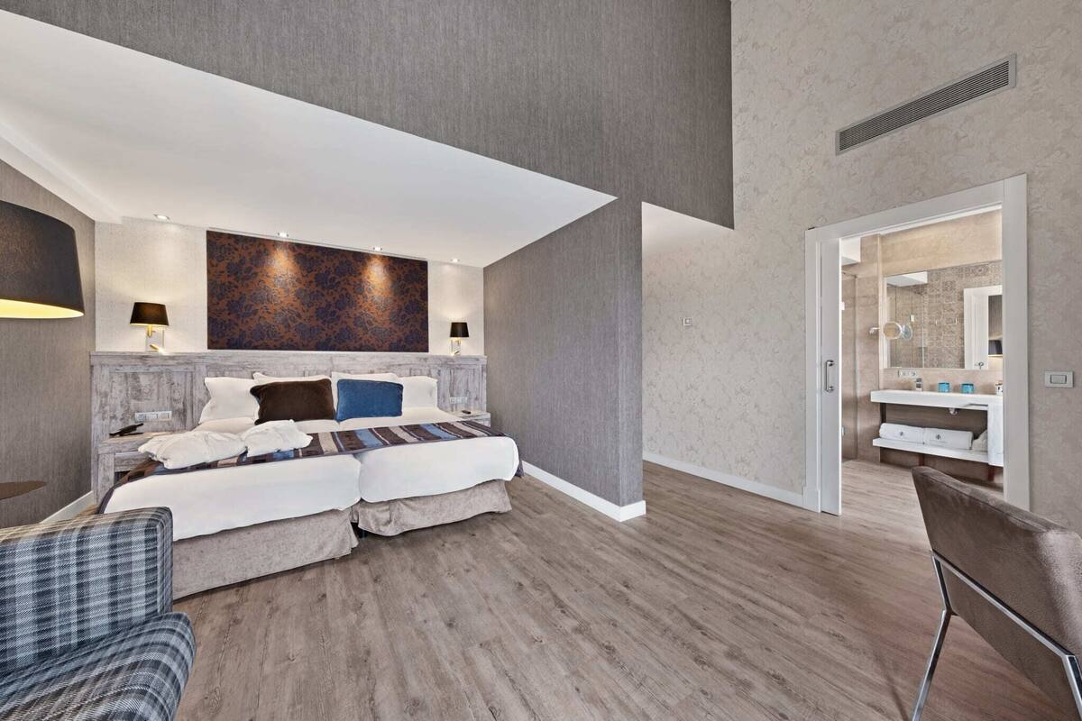 A modern hotel room with a large bed, a seating area, and a bathroom with a vanity and mirror.
