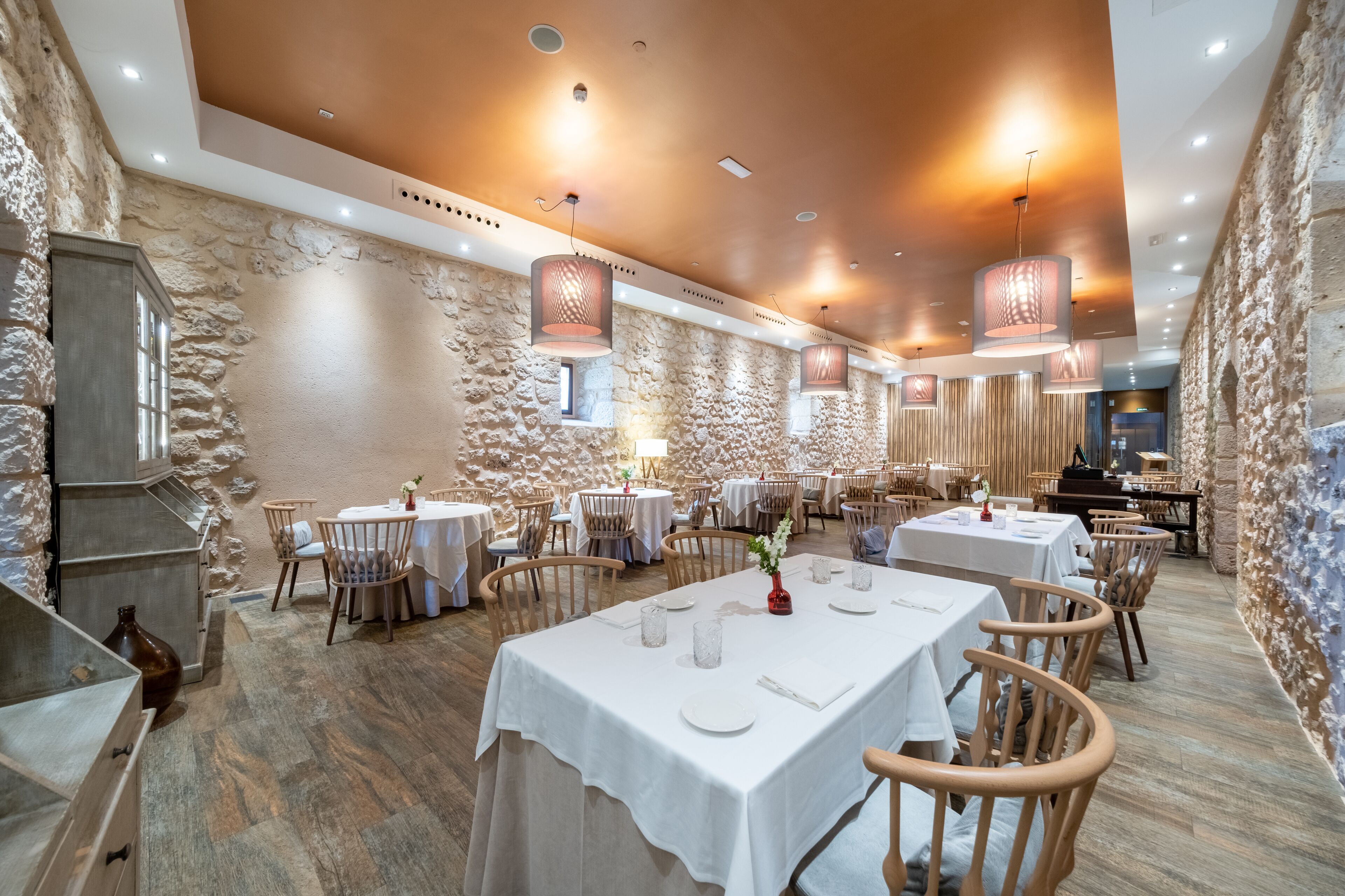 Ein Restaurant mit Steinsäulen, Holztischen und hängenden Lampen.
